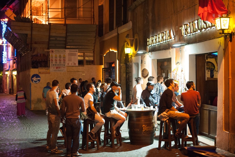 People at barrel tables outside Birreria Trilussa beer pub at night, Trastevere, Rome