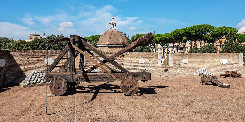 Reconstructed catapult and stacked stone cannonballs on the ramparts of Castel Sant'Angelo with the dome of St Peter's behind, Rome