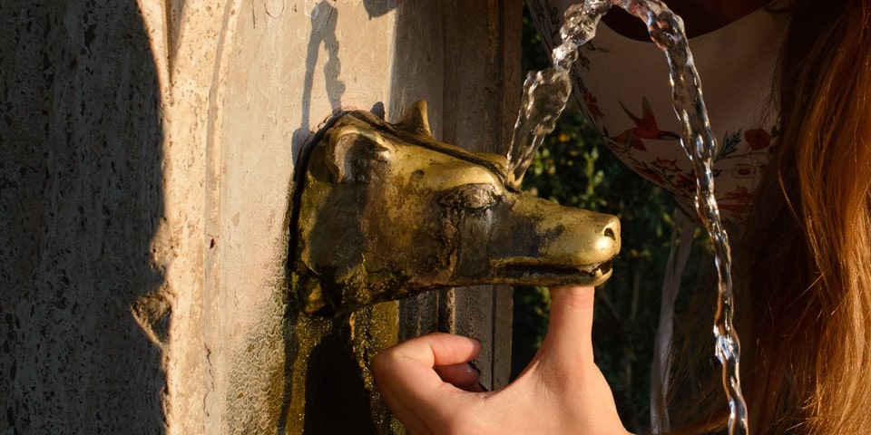 Finger covering the main outlet of a Villa Pamphilj drinking fountain to direct water through its upper hole